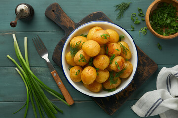 Fresh boiled new or young potatoes with butter, fresh dill and onions in white bowl on old rustic wooden background. Tasty new boiled potatoes. Top view.