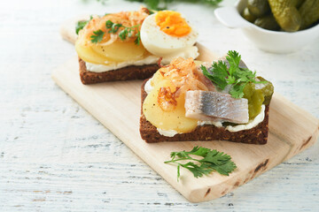 Open sandwich or smorrebrod with rye bread, herring, eggs, caramelized onions, parsley and cottage cheese on old wooden rustic table backgrounds. Danish or Scandinavian traditional food snack lunch.