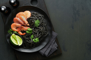 Black spaghetti pasta shrimp on black plate on dark concrete table background. Squid ink pasta with...