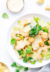Gourmet Caesar salad with shrimp, iceberg and lettuce, croutons, parmesan cheese and caesar dressing. White table background, top view