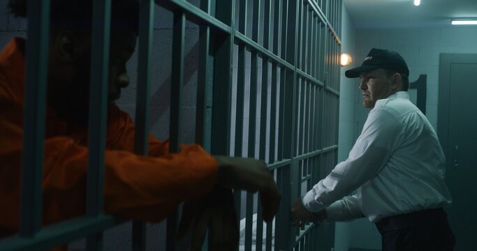 Warden brings guilty prisoner in jail cell and takes off handcuffs. African American man serves imprisonment term in correctional facility or detention center. Murderer in prison cell.