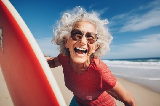 fit senior women having fun surfing Sporty woman training with surfboard on the beach - Elderly healthy people lifestyle and extreme sport concept