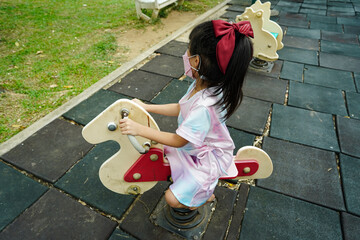 Asian little child, girl 4 years old alone plays in dress on rocking horse at playground, happy...