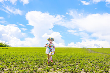 flag of Ukraine is on the shoulders of a little Ukrainian girl. Happy Ukrainian child in free Ukraine without war runs along a rural road in a field of farm soybean. International Mother Language Day.