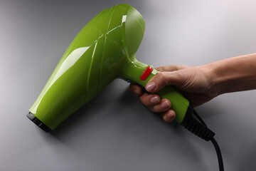 Woman hand holds bright green hair dryer on gray background. Choosing quality hair dryer