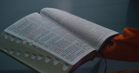 African American prisoner in orange uniform reads Bible in prison cell. Male criminal serves...