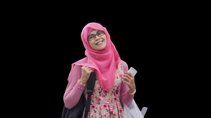 Close up portrait of smiling young Muslim woman wearing pink hijab and dress with red rose flower motif and black backpack holding phone. Happy and cheerful expression.