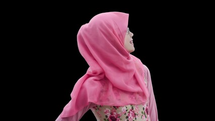 Close up portrait of smiling young Muslim woman wearing pink hijab and dress with red rose flower motif looking to her left. Happy and cheerful expression.