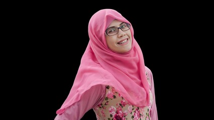 Close up portrait of young Muslim woman wearing pink hijab and dress with red rose flower motif and eyeglasses. Smiling and happy expression.