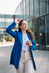 Vertical view of modern businesswoman in blue suit using mobile phone. Looking away. 