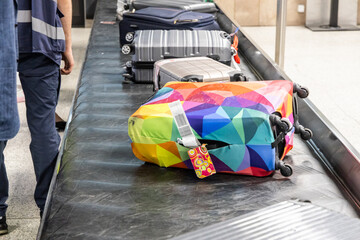 Luggage with cover in striking coloir on airport arrival conveyer belt stand out from other luggages