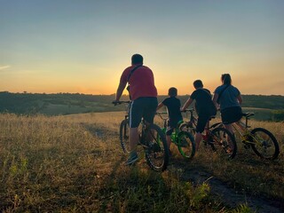 Family cyclists travel on the road at orange sunset