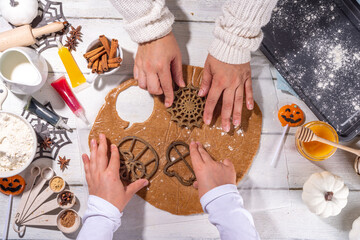 Cooking baking Halloween gingerbread cookies. Preparing for Halloween party holiday, mom and child cook together, make cut homemade funny cookies with molds in form of holiday symbols and monsters  - obrazy, fototapety, plakaty