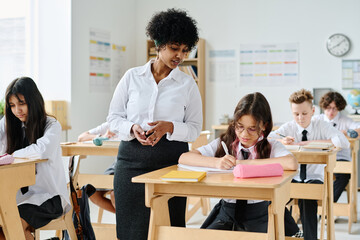 African American teacher having lesson with pupils at school while they sitting at desk and making notes in notebooks
