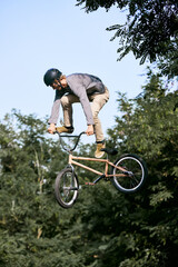 Fototapeta na wymiar Full-length dynamic image of young guy riding sport bicycle, bmx. Jumping high, doing tricks, training outdoors in park. Concept of active lifestyle, sport, extreme, dynamics, hobby