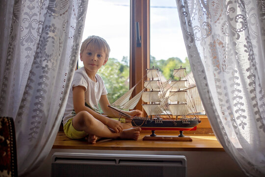 Cute blond child, boy, playing at home with big ship on the window