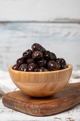 Black olives at wooden bowl. Olives on a white wood background. Mediterranean food. vegan food
