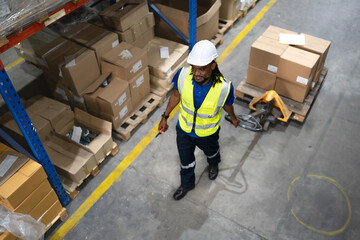 Multiracial man pulling hand pallet truck loading package boxes stacked in shipping warehouse. Worker moving merchandise from storage shelf by hand lift pallet jack. Delivery goods, cargo transport.