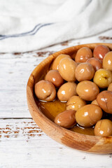 Scratched green olive at wooden bowl. Green olives on a white wood background. Mediterranean food. vegan food. Close up