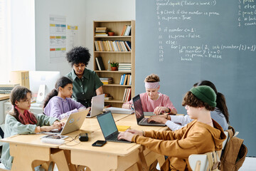 Group of school children studying IT together with teacher in the classroom