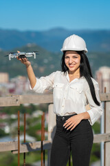 Smiling beautiful female geodesist engineer in a white helmet holds a drone at arm's length on a...