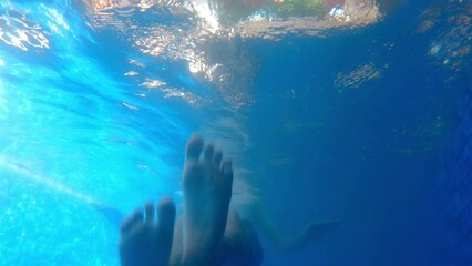 Cute funny adult male moving his legs like a duck underwater. Having fun leisure time in blue swimming pool on summer vacation. Film grain pixel texture. Young male person using feet as flippers. 