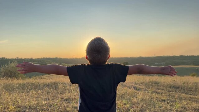 Silhouette of a cute boy, on a warm summer evening and dreaming about flying. Silhouette of a boy in a sunset setting with arms in the air feeling happy and free. 