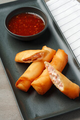 Deep fried shrimps spring roll on black plate with sauce