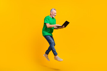 Fototapeta na wymiar Full length profile portrait of excited carefree man jumping hold use netbook coworking isolated on yellow color background