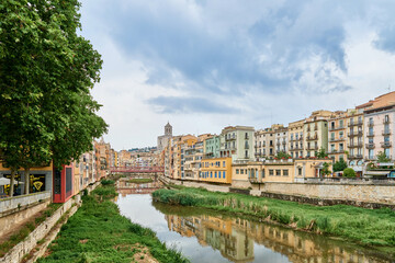 Fototapeta premium Colorful yellow and orange houses and bridge Pont de Sant Agusti reflected in water river Onyar, in Girona, Catalonia, Spain. Church of Sant Feliu and Saint Mary Cathedral at background. BRIDGE in the