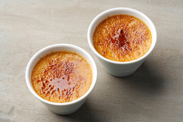 Creme brulee with caramel in two white bowls on gray background