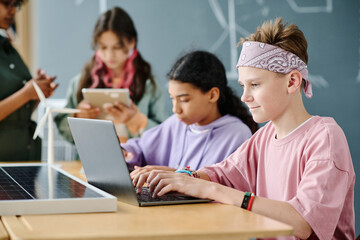 Schoolboy sitting at table in the classroom and working online on laptop