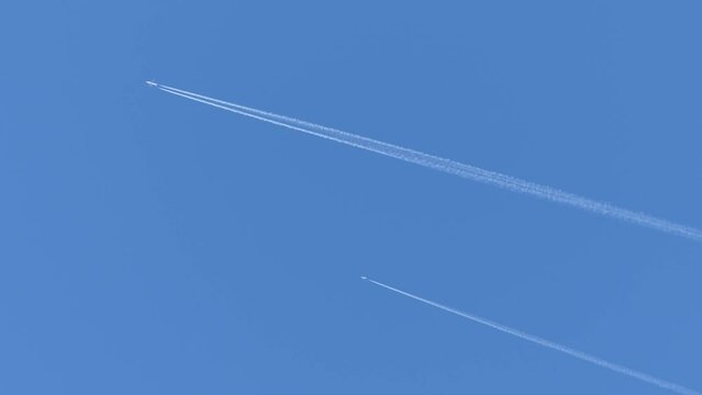 Two planes flying in parallel against the background of a blue sky and leaving a trails of condensation clouds in the form of white lines - real time.