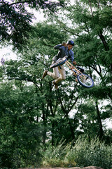 Fototapeta na wymiar Summer activity. Young sportive man riding bmx bike in forest, doing dangerous and difficult tricks, jumping with bicycle. Concept of active lifestyle, sport, extreme, dynamics, hobby, freestyle