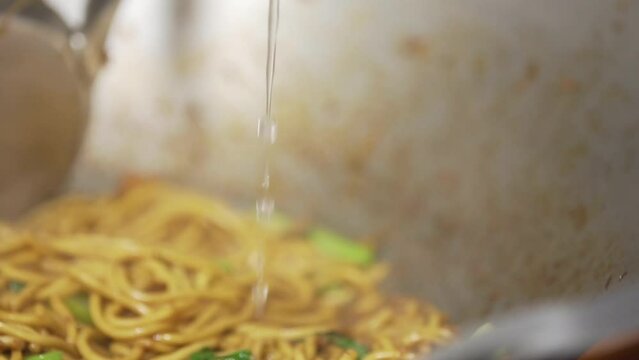 The chef is adding the broth to the Hokkien noodles in a steaming hot wok. Phuket local food