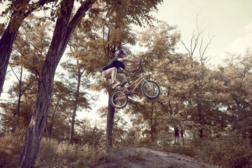 Young man in helmet training outdoors in forest, riding bmx bike, doing tricks. Autumn ride, extreme man. Concept of active lifestyle, sport, extreme, dynamics, hobby, freestyle