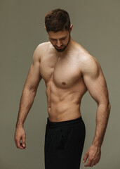 Slim muscular male model at gray background. Fitness shirtless guy in black sport pants posing in studio