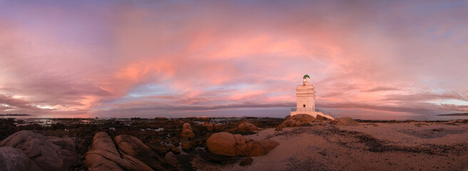 Lighthouse built on coastal rocks standing in the sunset light