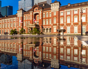 Reflection of the 1800s era red brick Tokyo Station building in water sprayed to cool the outside pavement on a hot summers day