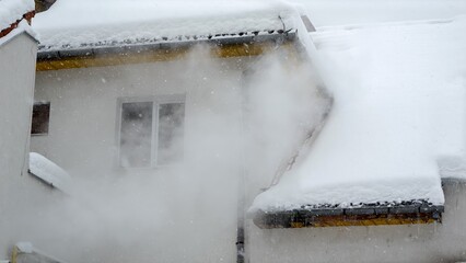 Smoke or water steam flowing from heating system of private house on snowy winter day. Concept of energy, ecology, heating and pollution