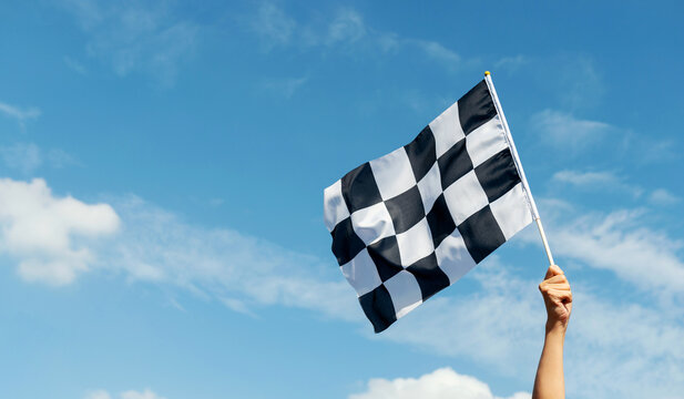 Checkered race flag in hand against blue sky