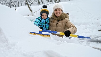 Woman and her baby son clearing snow from their car with a brush after a snowstorm. The concept of...