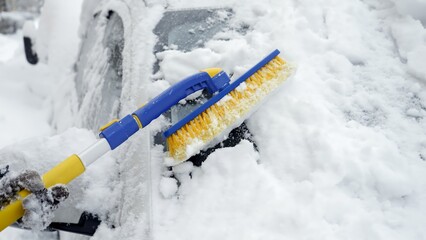 Close-up of a woman using a snow brush to clear snow off of her car's windshield. Concept of winter...