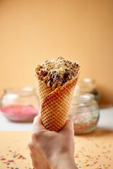 Vertical shot of a hand holding an icecream cone with sprinkles