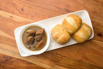 Plate of freshly-baked bread rolls and a serving of savory soup topped with succulent pieces of meat