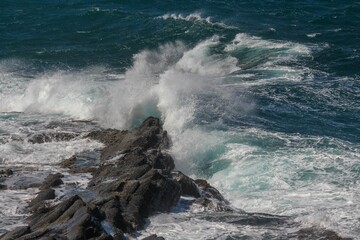Powerful ocean wave breaks against a rocky shoreline on a sunny day © Woodhicker_shots1/Wirestock Creators