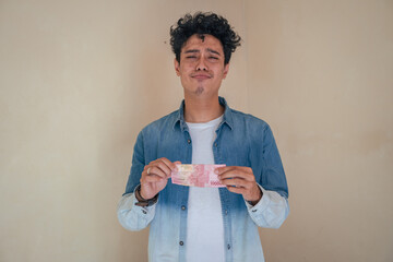 Young curly man wear denim clothes with sad expression, cause less money. The photo is suitable to...