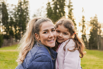 Happy mother and little daughter having tender moment while smiling on camera during trekking day in nature