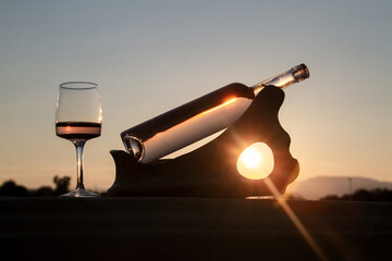 Une bouteille et un  verre de vin rosé  posés sur un support en bois au couché de soleil 