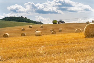 Fototapeta na wymiar Straw bales in the summer sun on a hillside in Hungary with a tractor in the background.